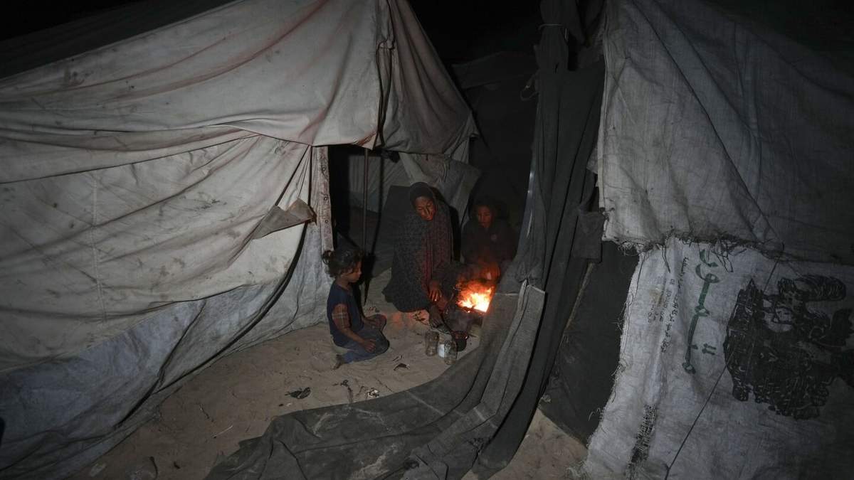 Shireen Daifallah, que fue desplazada con sus hijos del norte de Gaza, revisa el fuego junto a su tienda de campaña en un campamento de desplazados en Deir al-Balah, Franja de Gaza