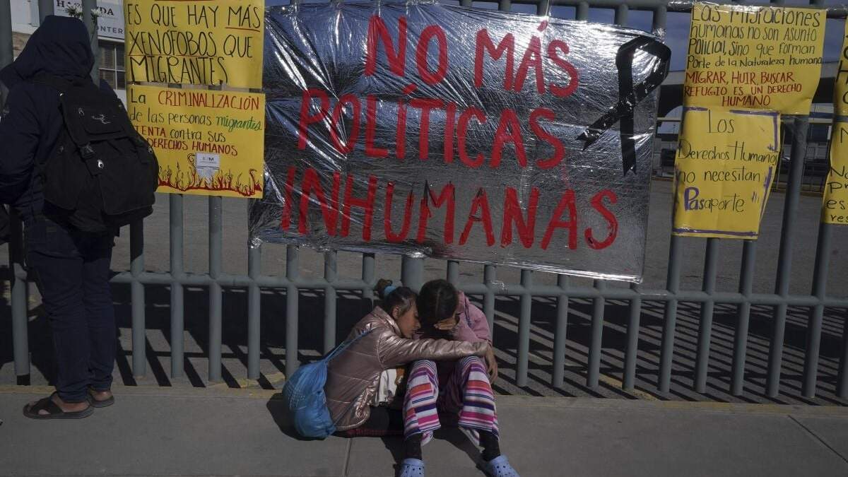 Dos hermanas venezolanas se consuelan sentadas en una vereda ante un centro de detención de migrantes donde docenas de migrantes que temían ser deportado prendieron fuego a las colchonetas, lo que provocó un incendio que mató a docenas de personas, en Ciudad Juárez, México, el martes 28 de marzo de 2023. El cartel dice "No más políticas inhumanas". ()