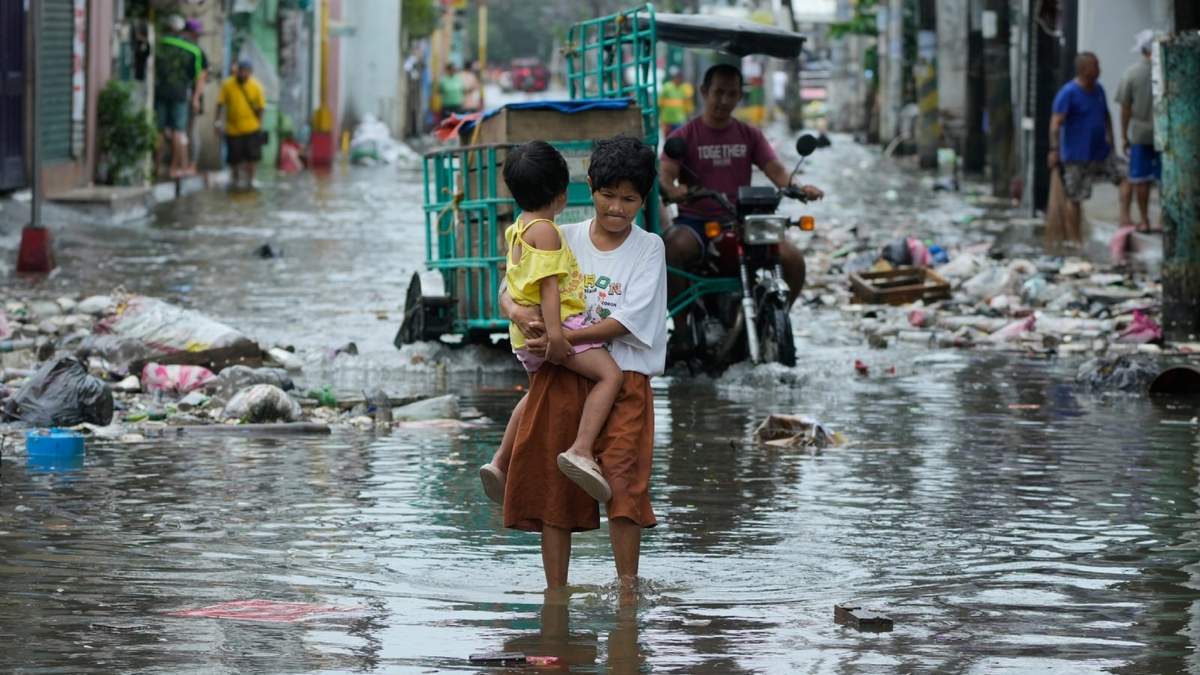 Una mujer y un niño cruzan una calle inundada por las tormentas del tifón Fung-wong y la marea alta el lunes 10 de noviembre de 2025 en Navotas, Filipinas
