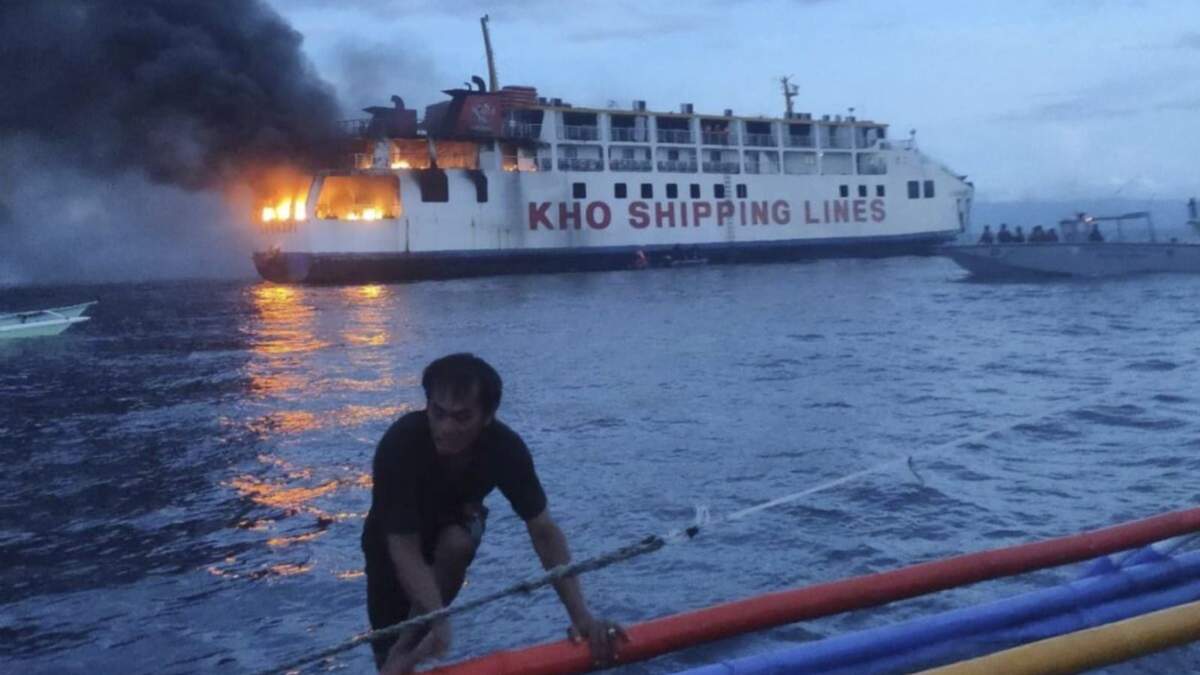 Un hombre empuja un bote cerca del ferry filipino M/V Esperanza Star que se incendia en aguas frente a Panglao, en la provincia Bohol, Filipinas