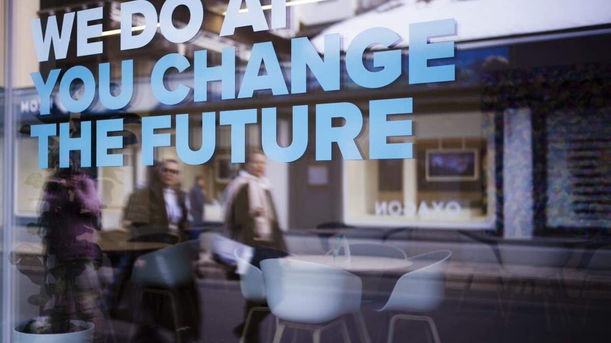Gente se refleja en una ventana con un eslogan sobre la inteligencia artificial antes del Foro de Economía Mundial en Davos, Suiza