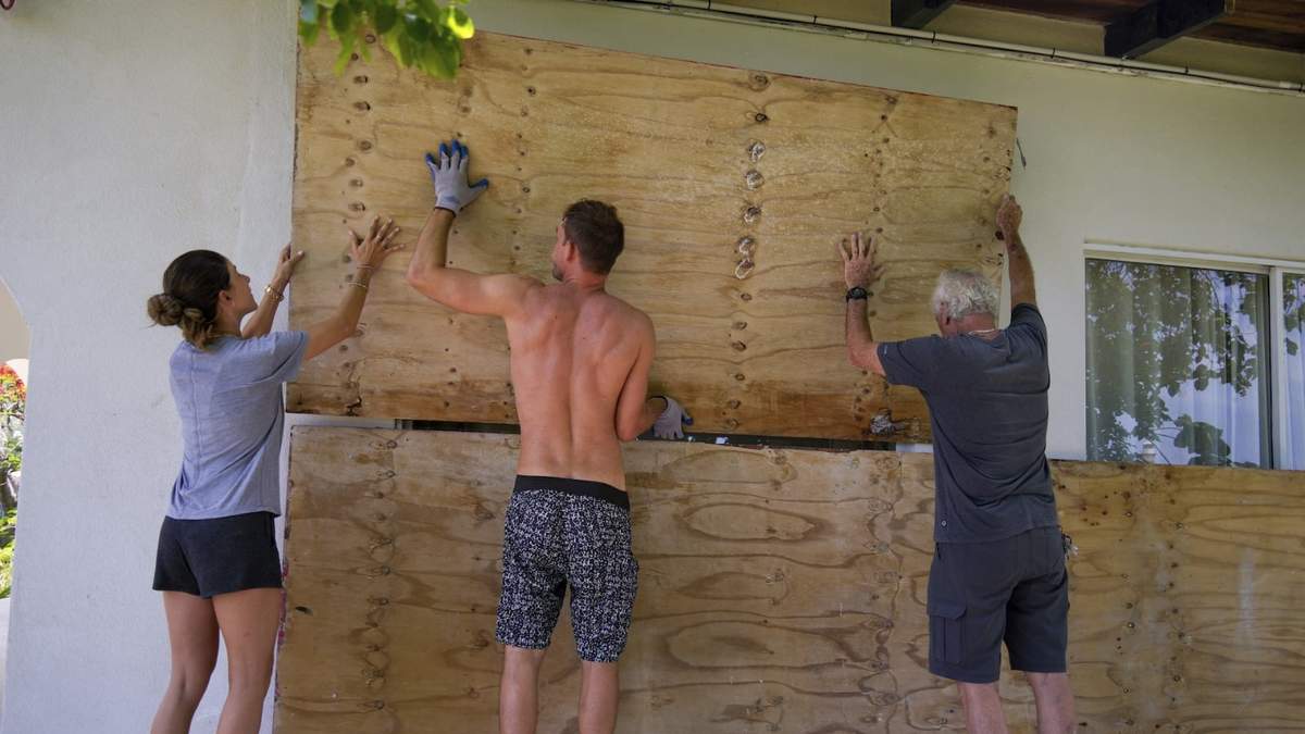 Tres personas cubren las ventanas de su hogar en preparación para la llegada del huracán Beryl en Bridgetown, Barbados.