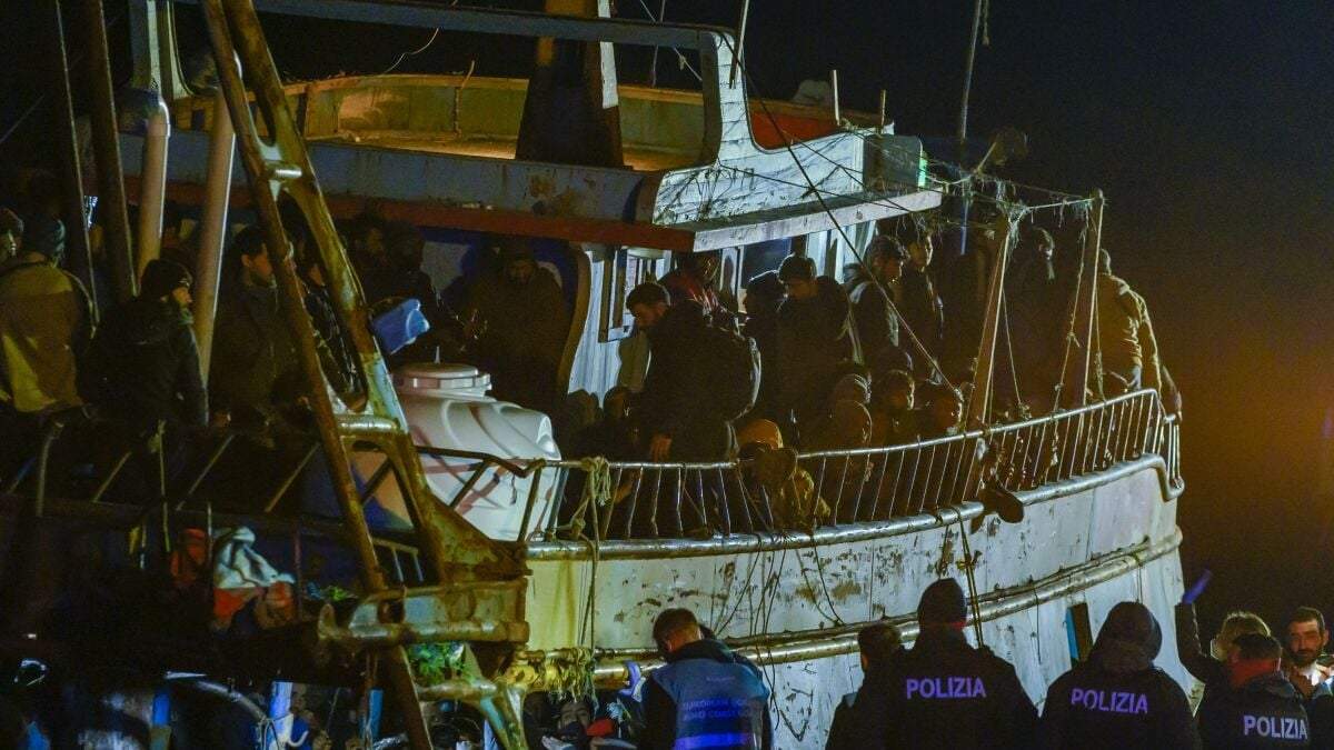 Varios policías, abajo, aguardan frente a un barco pesquero con unos 500 migrantes la madrugada del sábado en el puerto de Crotone, en el sur de Italia