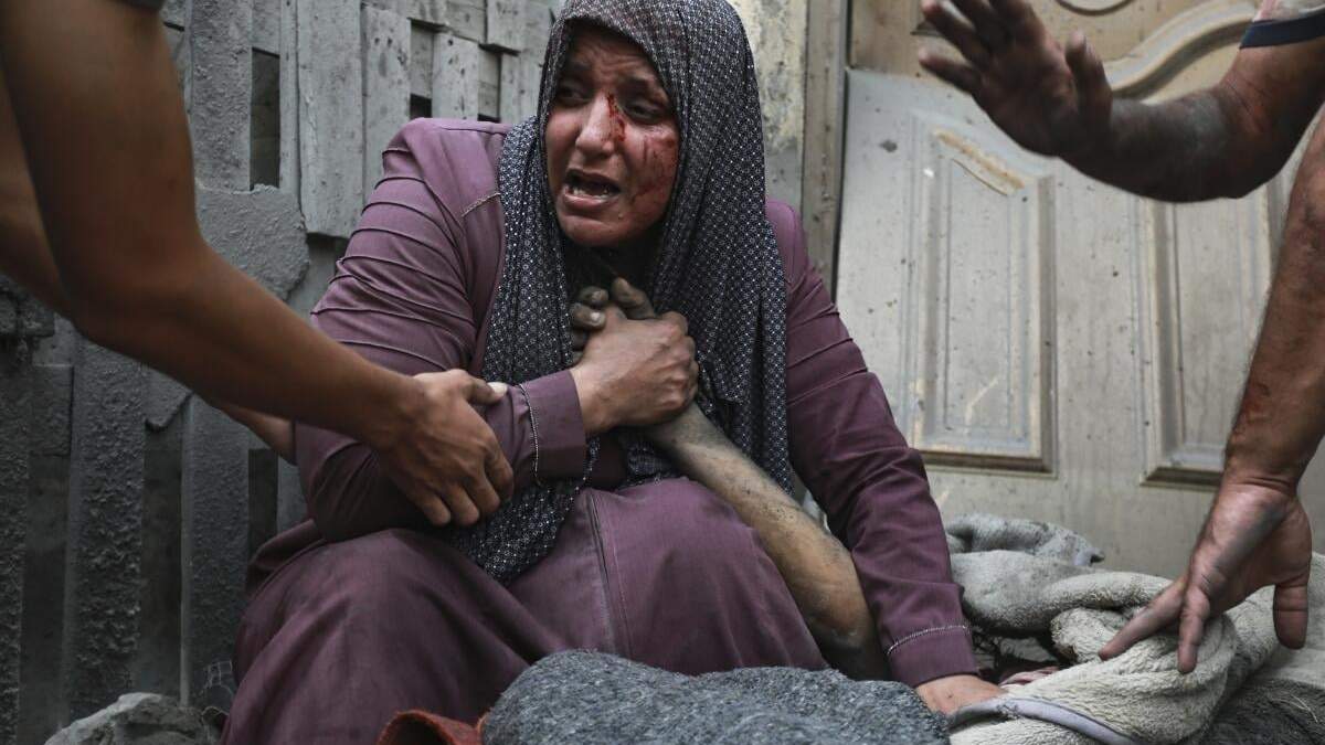 Una mujer palestina herida llora mientras sostiene la mano de su familiar muerto ante su casa tras ataques israelíes que golpearon su vecindario en Ciudad de Gaza