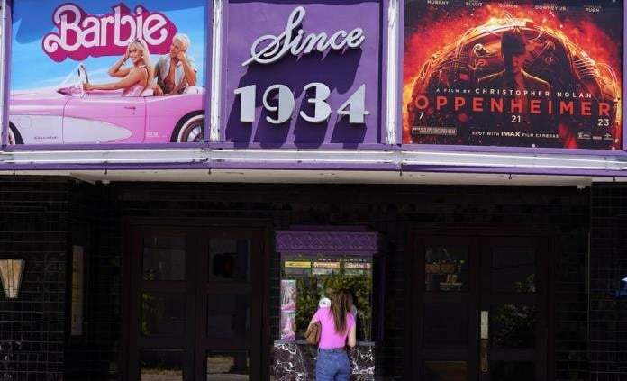 Una persona compra boletos de cine debajo de una marquesina con las películas "Barbie" y "Oppenheimer" en Los Ángeles