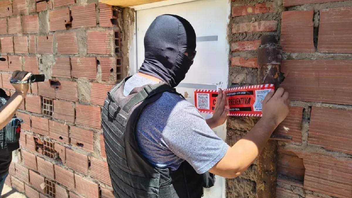 Un efectivo policial coloca la faja de clausura por segunda vez en la misma vivienda del barrio Otaño. Fuente: (Neuquén Informa)
