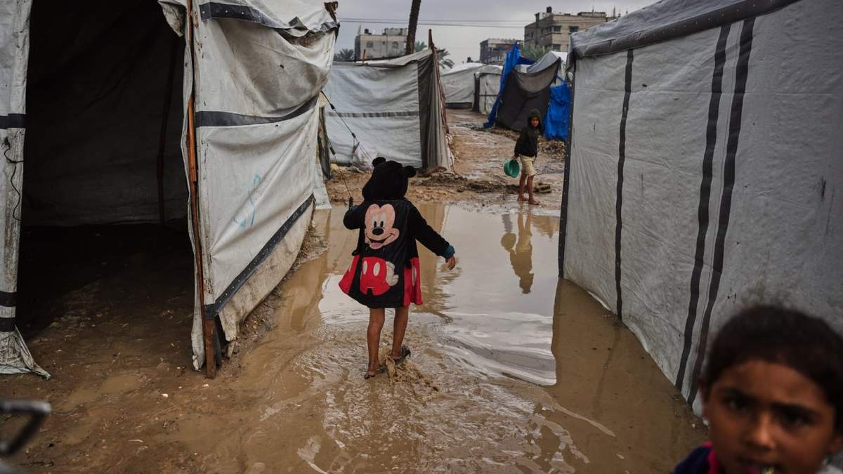 Niños palestinos caminan entre lodo en una zona de tiendas de campaña, luego de una fuerte lluvia en Deir al-Balah, Franja de Gaza, el 25 de noviembre de 2025