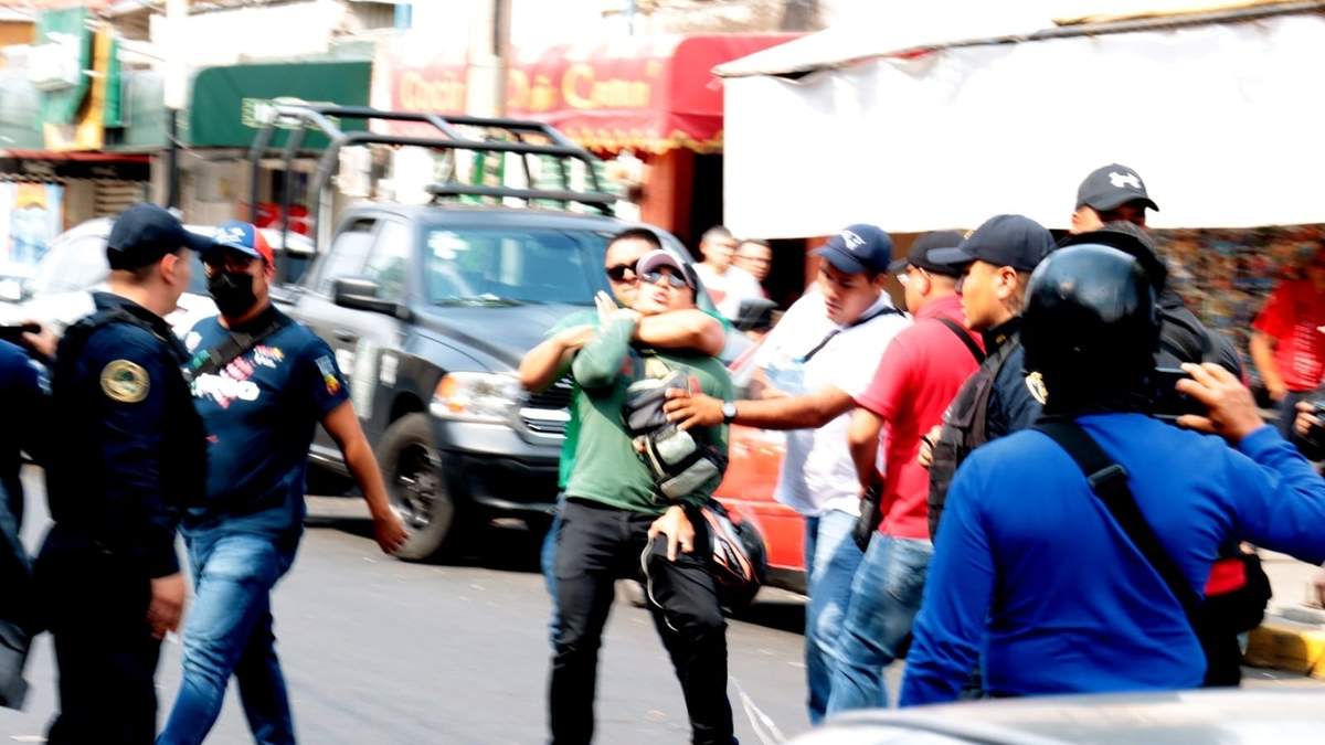 Un policía vestido de civil somete a un reportero mientras otro le roba sus pertenencias