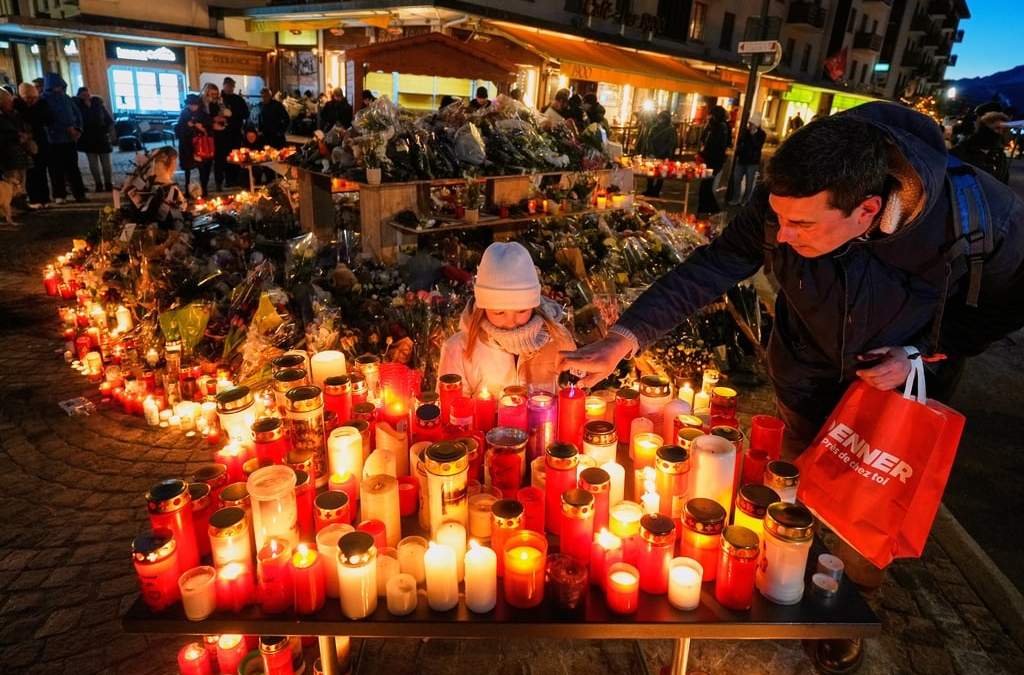 ARCHIVO - Una niña observa mientras un adulto coloca una vela en el exterior del bar Le Constellation, en Crans-Montana, en los Alpes suizos, el 3 de enero de 2026, donde un devastador incendio causó decenas de muertos y heridos durante la celebración de Año Nuevo