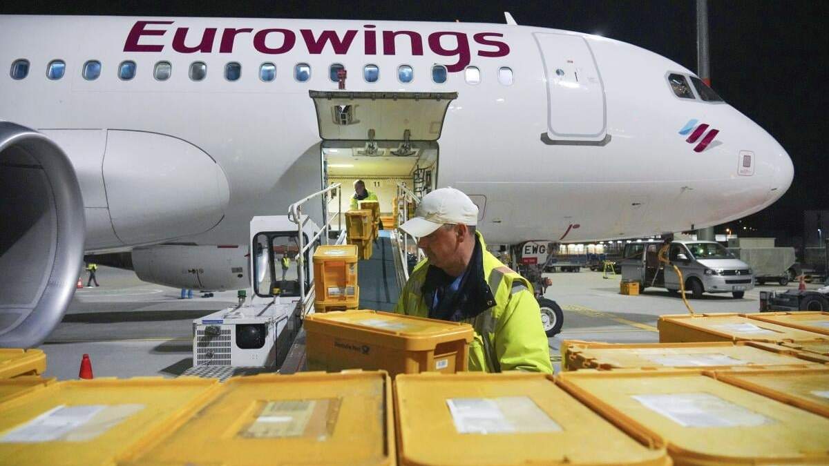 Empleados de WISAG cargan un Airbus A320-214 de Eurowings que se dirige a Stuttgart con cajas de plástico cargadas de cartas y paquetes, en el aeropuerto Berlin Brandenburg, en Schönefeld, Alemania