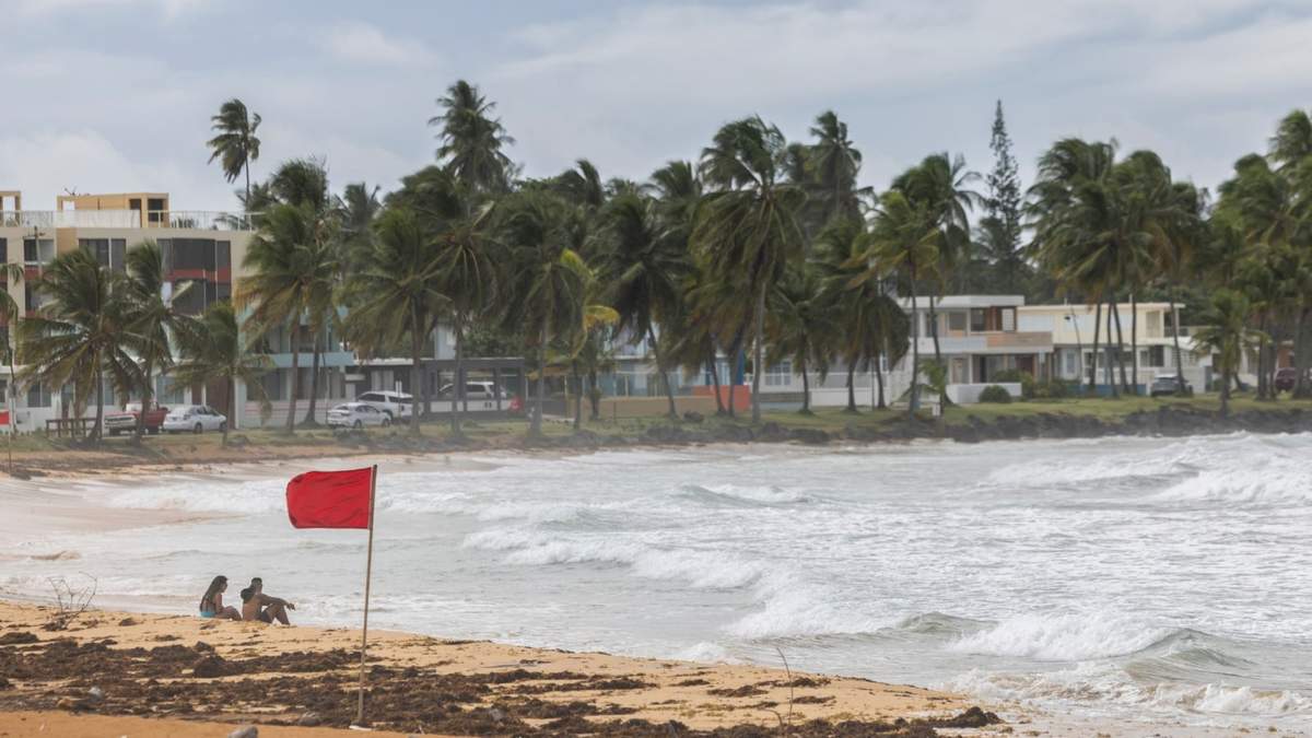 Turistas sentados en la playa La Pared mientras la tormenta tropical "Ernesto" pasa por Luquillo, Puerto Rico