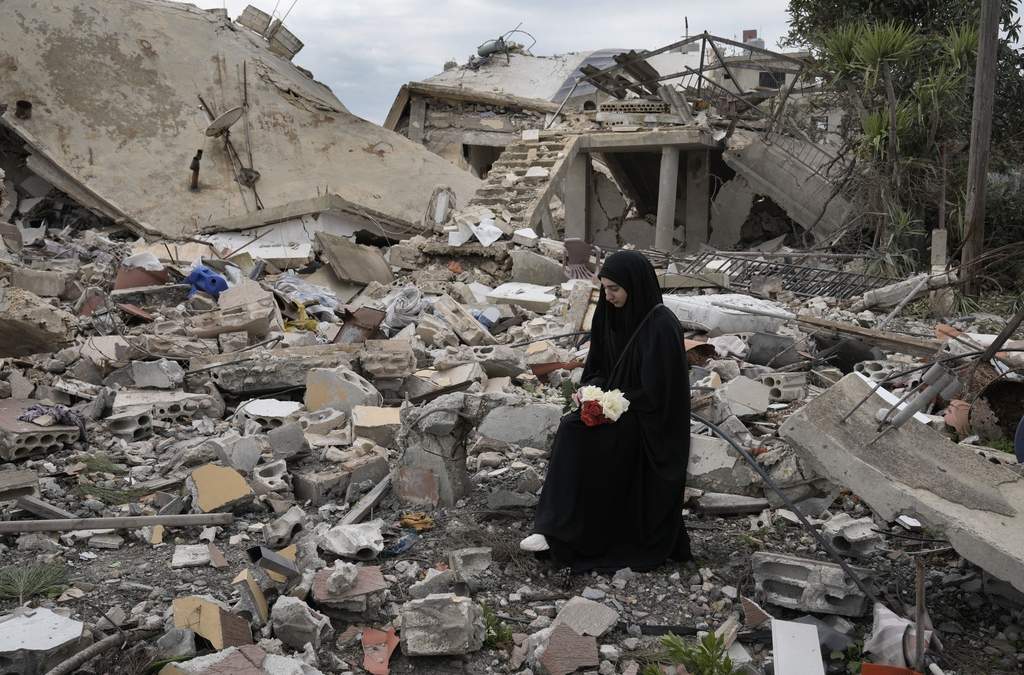 Una mujer libanesa sostiene un ramo de flores mientras permanece sentada entre los escombro de una casa destruida tras una ofensiva aérea y terrestre de Israel, en Aita al-Shaab, una aldea libanesa que hace frontera con Israel, en el sur de Líbano