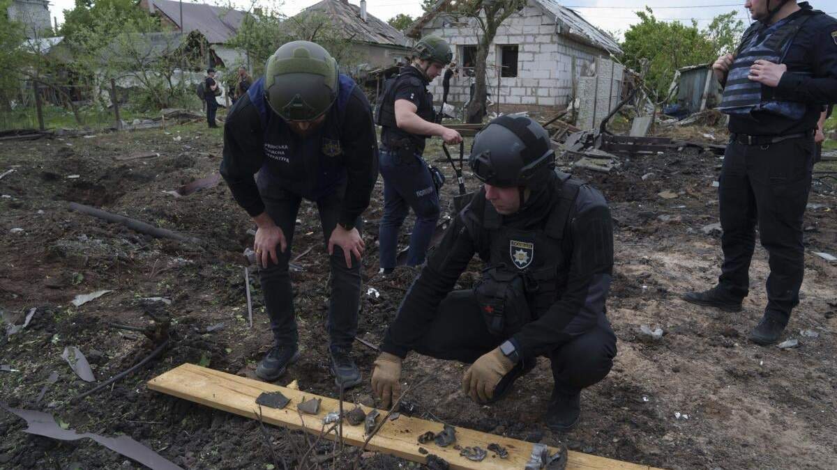 Un policía ucraniano y un fiscal de crímenes de guerra analizan fragmentos de una bomba frente a una residencia dañada después de un ataque aéreo ruso contra un vecindario residencial