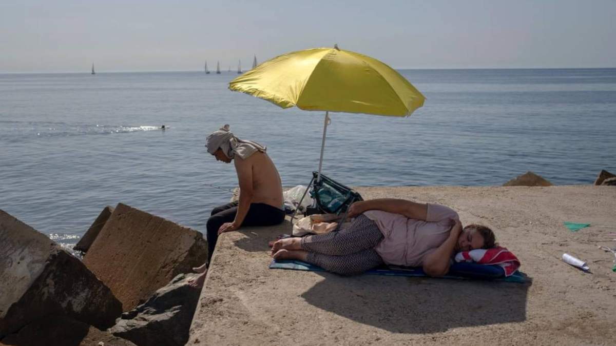Una mujer duerme bajo un paraguas en un rompeolas frente al mar Mediterráneo en Barcelona, ??España