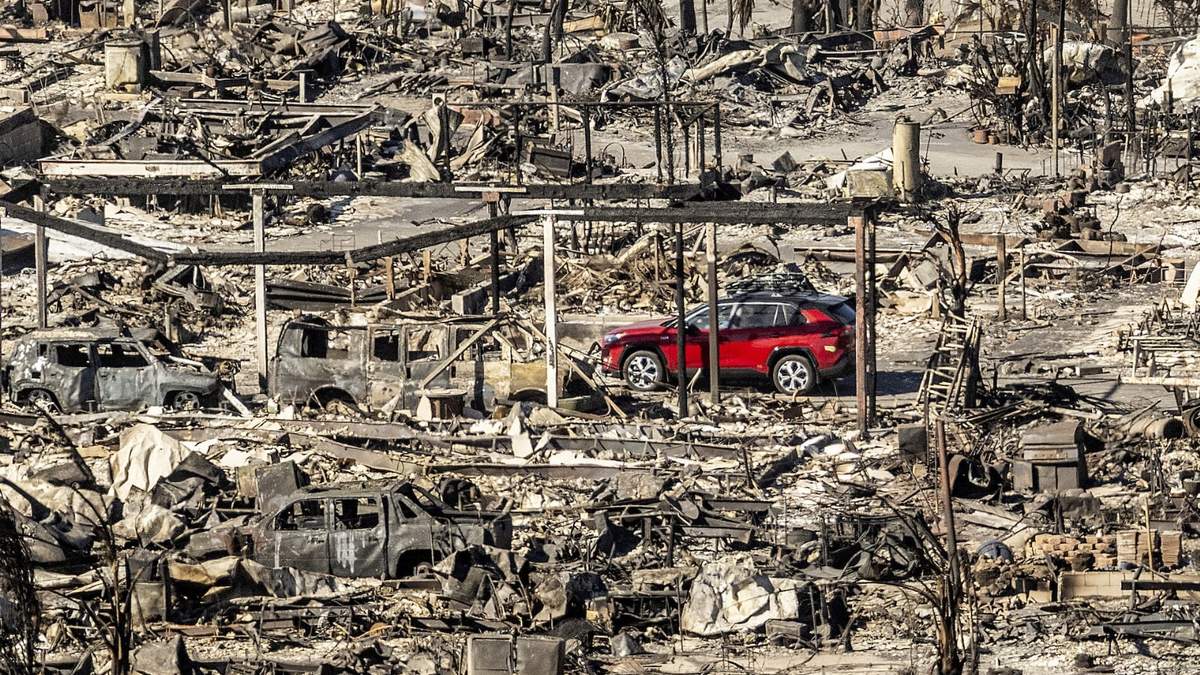 Un automóvil pasa junto a casas y vehículos destruidos por el incendio de Pacific Palisades