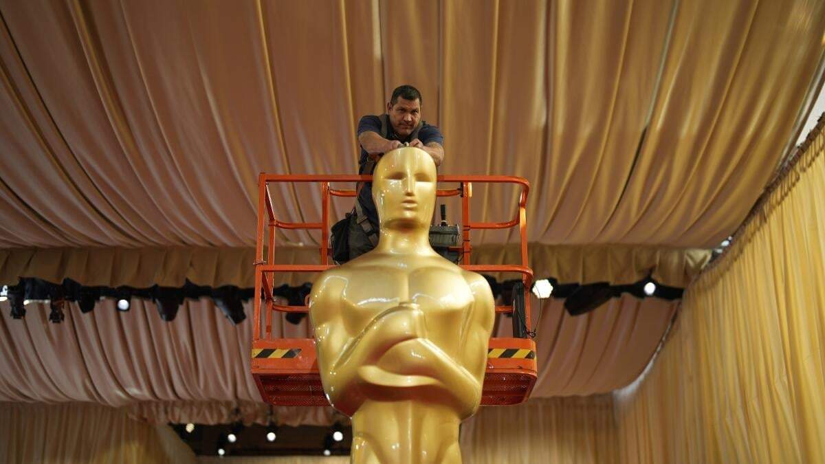 Un trabajador ayuda a colocar una estatua de los Oscar en la alfombra roja previo a la 96a entrega de los Premios de la Academia