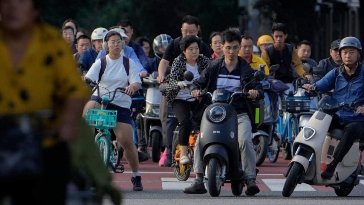 Un grupo de personas, en moto y bicicleta, esperan a que un semáforo se ponga verde en un cruce durante la hora punta de la mañana, en Beijing, el 13 de septiembre de 2024