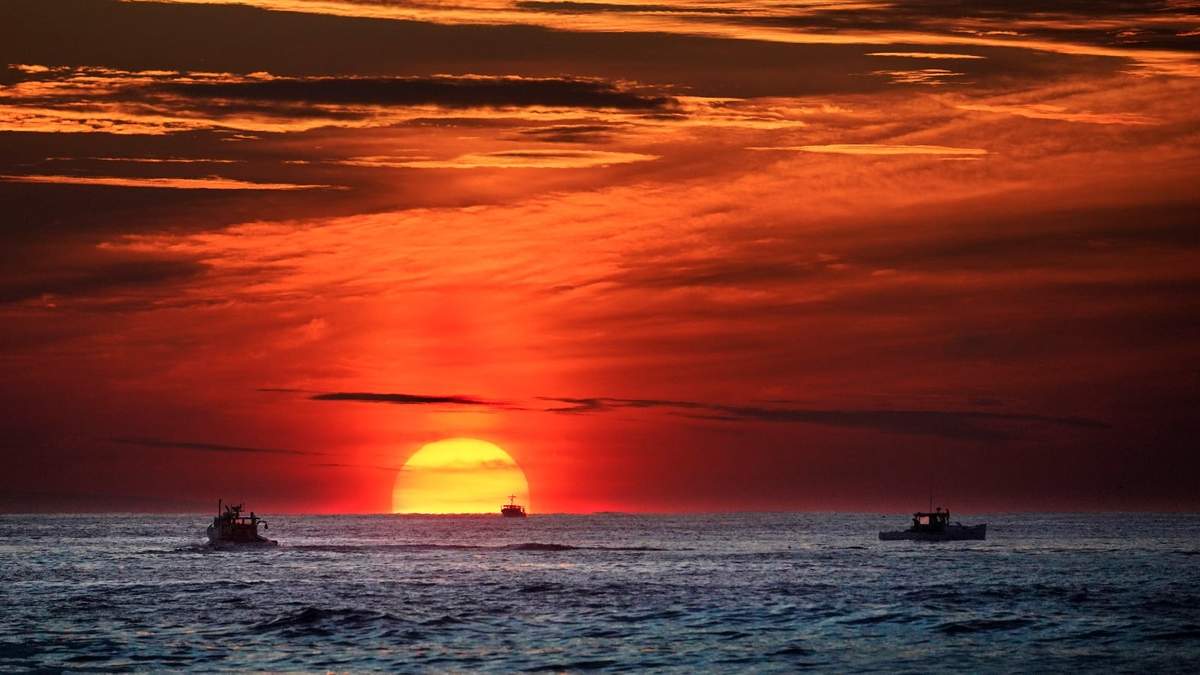 El sol se levanta en el horizonte del mar donde alcanzan a divisarse embarcaciones pesqueras en el océano Atlántico frente a las costas de Kennebunkport, Maine