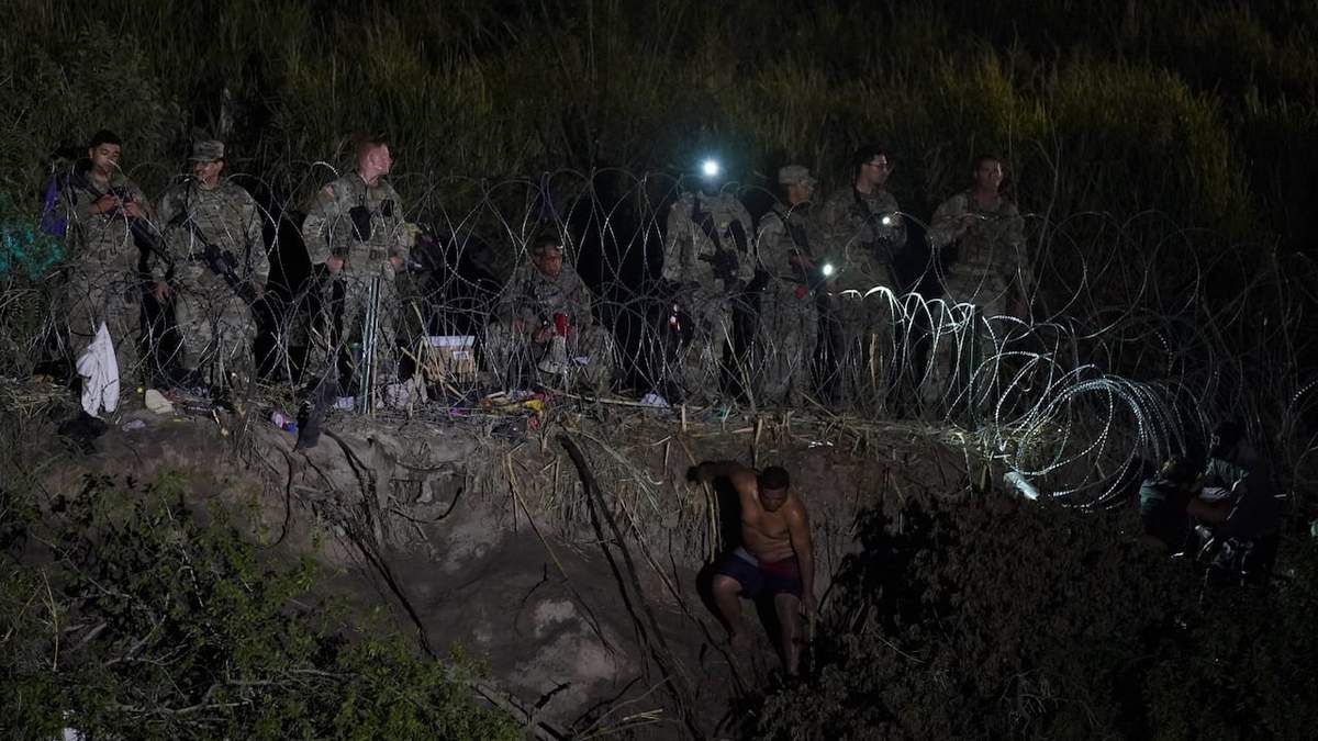 Los miembros de la Guardia Nacional de Texas se paran junto a un tramo de alambre de púas mientras los migrantes intentan cruzar a los Estados Unidos a orillas del Río Grande