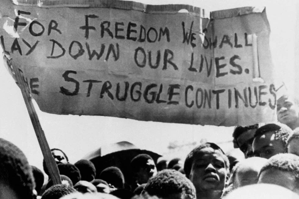 Estudiantes negros en Johannesburgo, Sudáfrica, en el municipio de Soweto, donde se congregaron tras el funeral de un estudiante negro de 16 años que murió en prisión el 18 de octubre de 1976, ondean una pancarta.