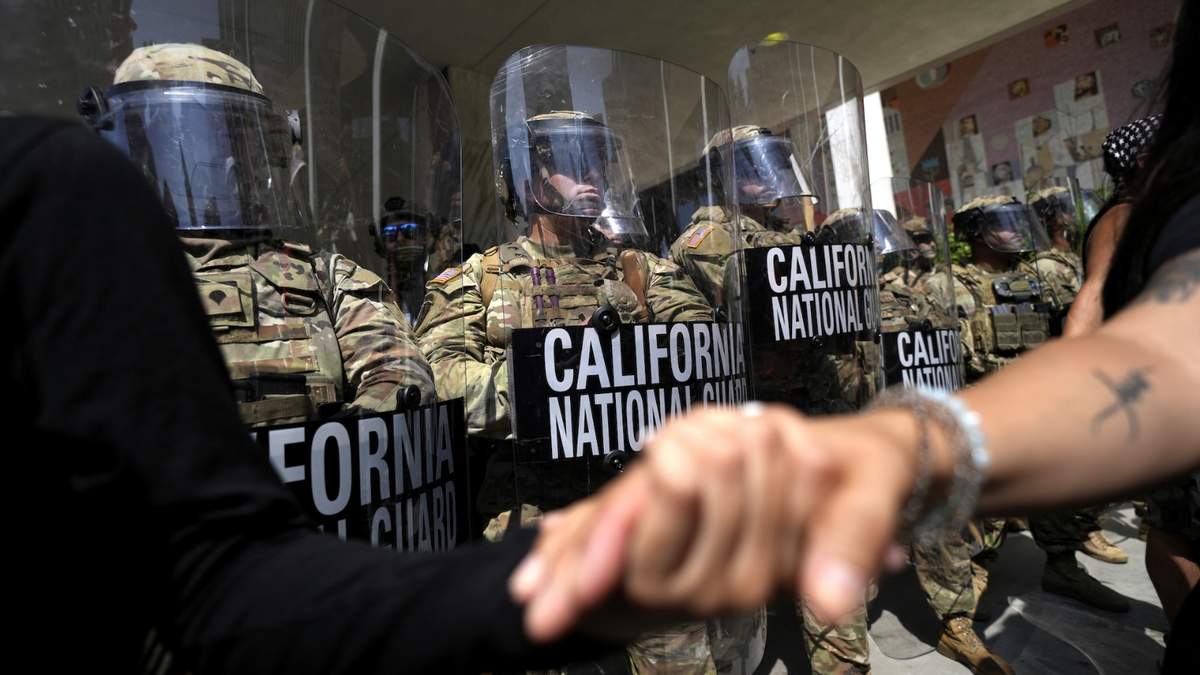 Manifestantes se toman de las manos frente a soldados de la Guardia Nacional de California el lunes