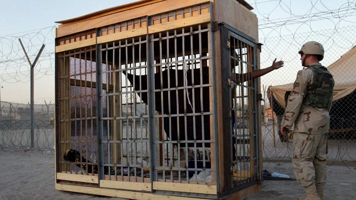 Un detenido en una celda de confinamiento solitario al aire libre habla con un soldado en la prisión de Abu Ghraib en 2004