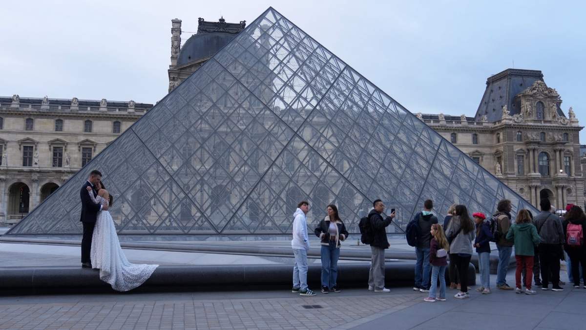 Una pareja de novios se abraza mientras los visitantes hacen fila para entrar al museo del Louvre tres días después de que joyas históricas fueran robadas en un audaz robo a plena luz del día, el miércoles 22 de octubre de 2025 en París