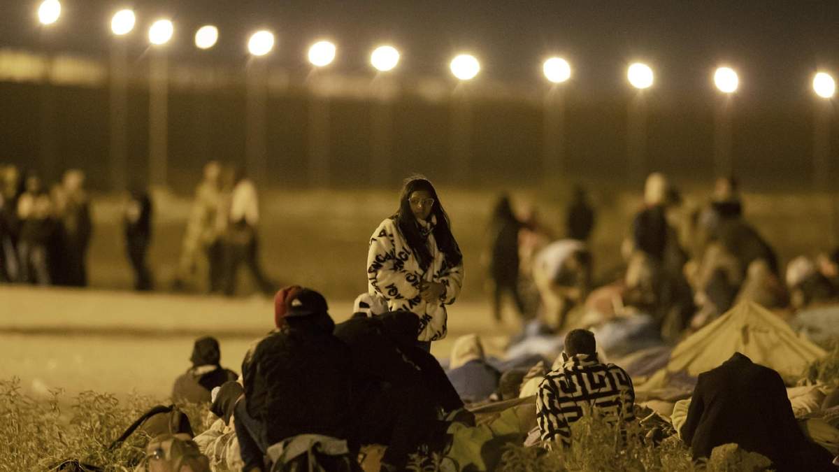 Migrantes esperan en una puerta en el muro fronterizo tras cruzar desde Ciudad Juárez, México, a El Paso, Texas