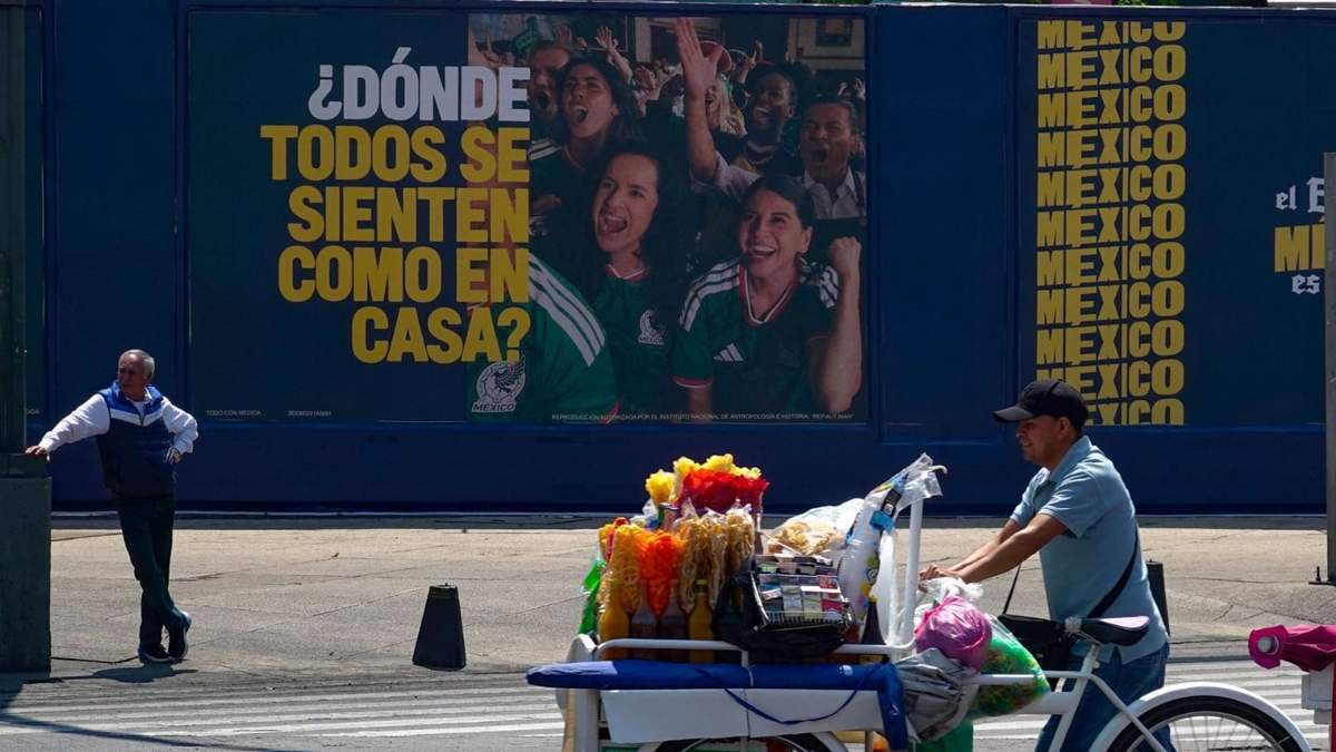 Un vendedor de frituras empuja su triciclo frente a una publicidad alusiva al Mundial de Futbol 2026 que se celebrara en nuestro país