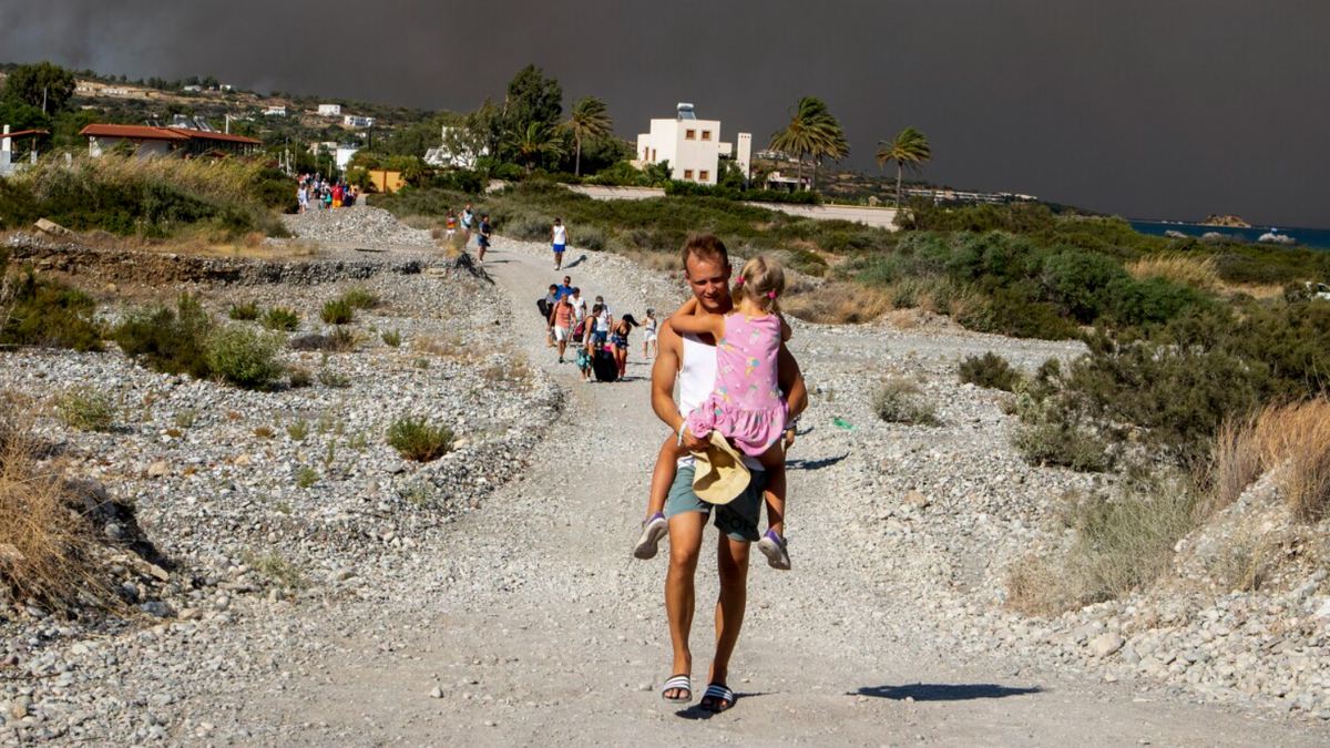 Un hombres lleva a una niña al abandonar la zona donde arde un incendio forestal en la isla de Rodas, Grecia