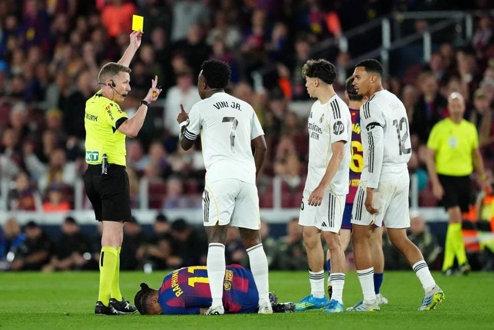 El árbitro Alejandro José Hernández Hernández muestra una tarjeta amarilla a Trent Alexander-Arnold, del Real Madrid (derecha), durante el partido de la Liga española entre el FC Barcelona y el Real Madrid en Barcelona, ??España, el domingo 10 de mayo de 2026.