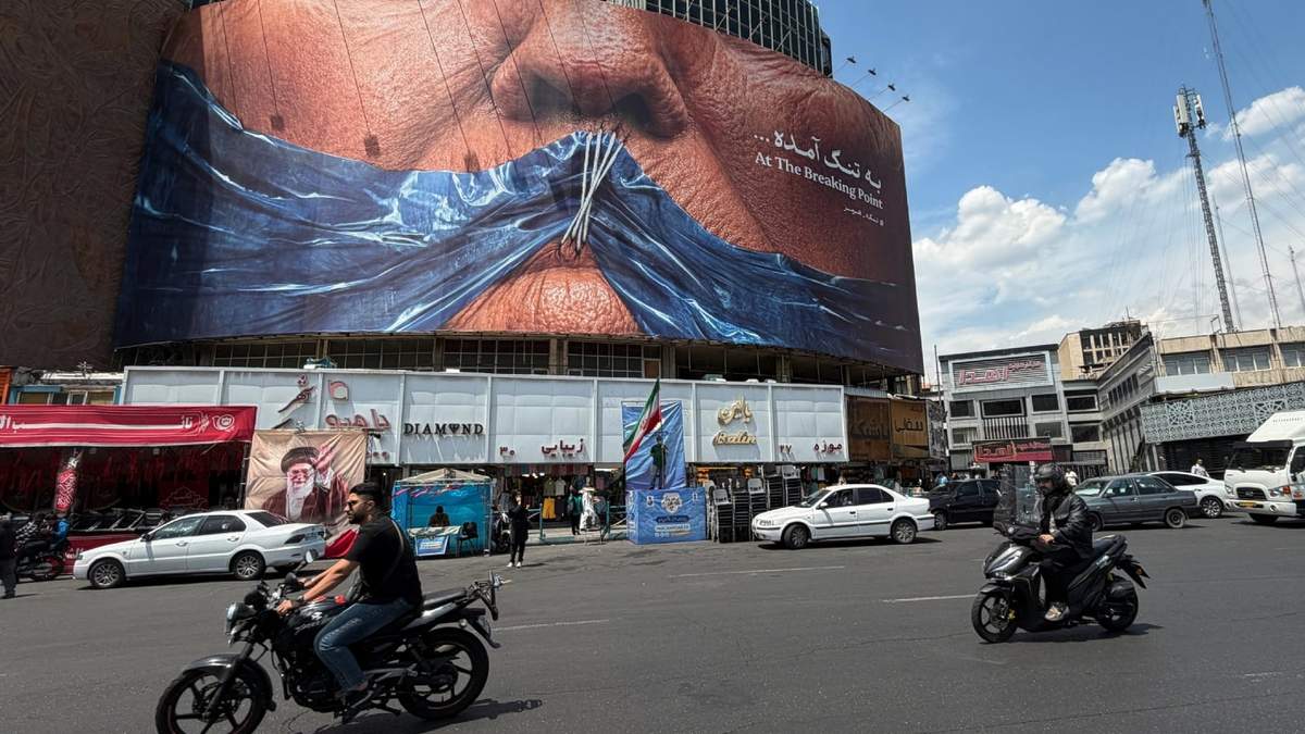 Vehículos circulan junto a una valla publicitaria con una imagen del estrecho de Ormuz y los labios cosidos del presidente estadounidense Donald Trump en una plaza del centro de Teherán, Irán, el sábado 2 de mayo de 2026
