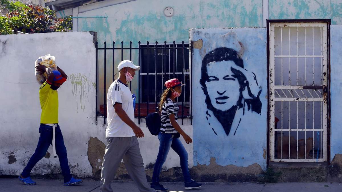 Personas usando tapabocas frente a un mural de Hugo Chávez, en Carabobo. Fuente: (Twitter)