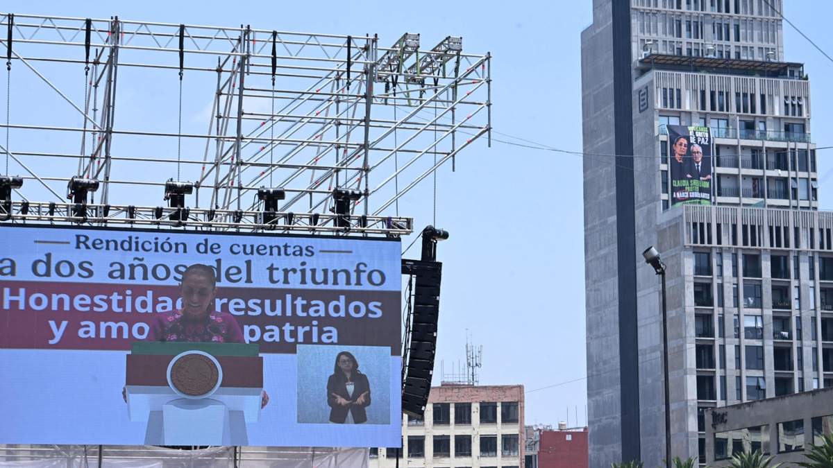 La presidenta Claudia Sheinbaum en una de las pantallas que transmitieron su mensaje. A un lado, una manta colocada por opositores