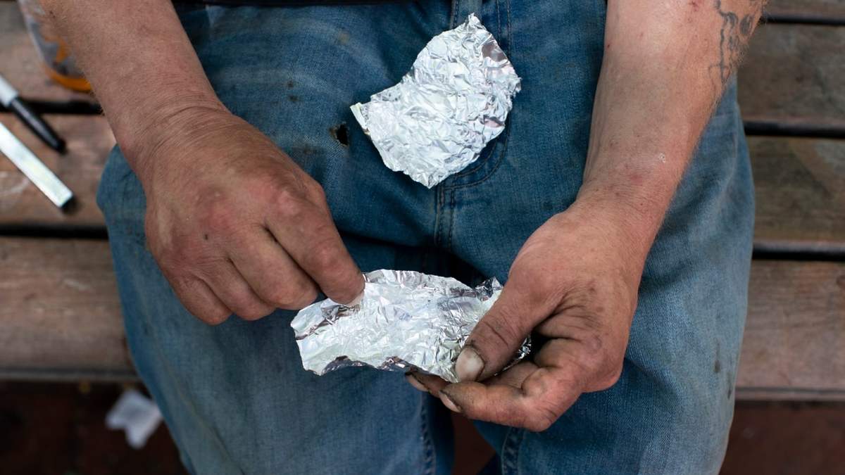 Un hombre se prepara para fumar fentanilo en la banca de un parque, en el centro de Portland, Oregon