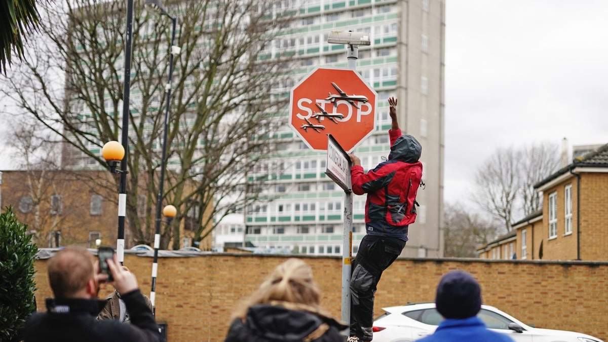 Una persona retira una obra de arte de Banksy que parece mostrar tres drones sobre un cartel de Stop que fue develado en la intersección de calles de Londres