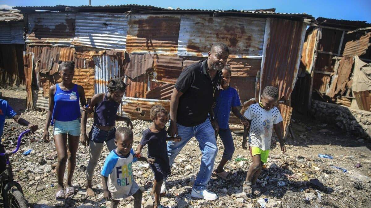 ARCHIVO - Jimmy Chérizier, un expolicía de élite conocido como Barbacue y que ahora dirige una federación de pandillas, camina de la mano de varios niños en una visita al distrito de La Saline en Puerto Príncipe, Haití