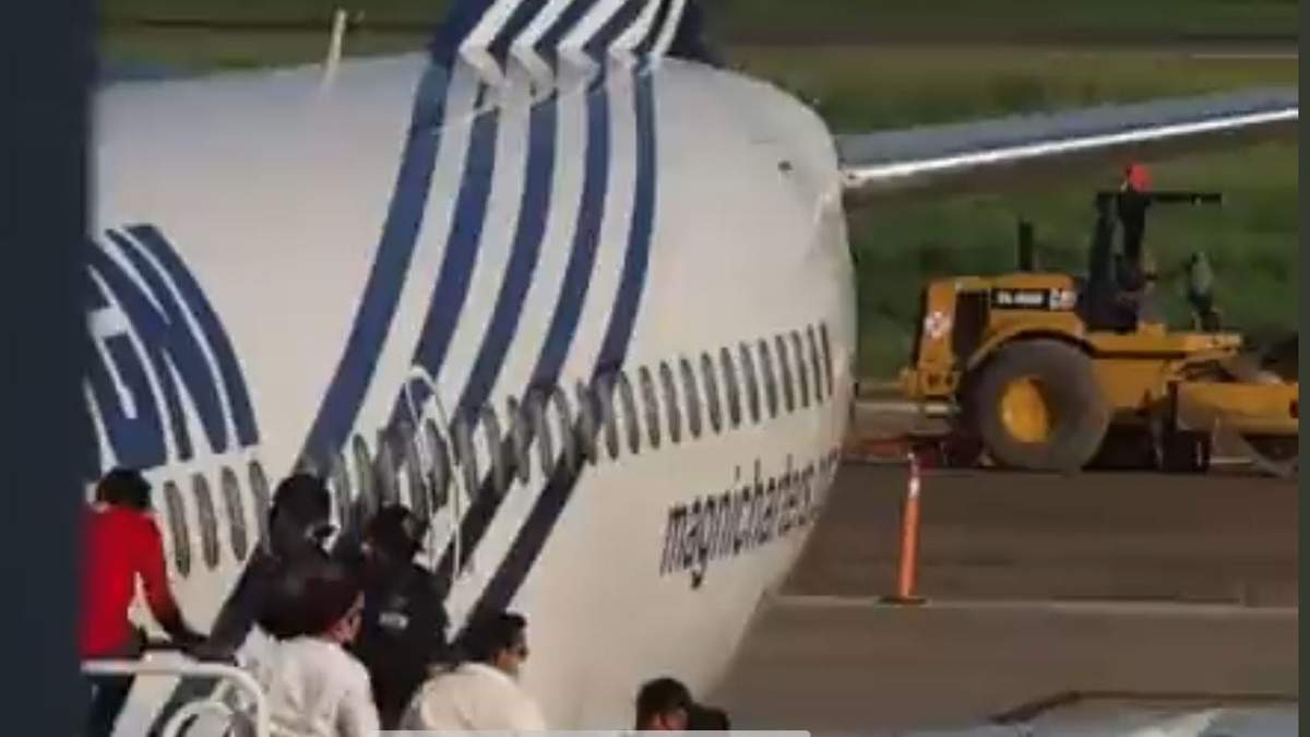 El migrante, con playera roja, salta de las escalinatas del avión