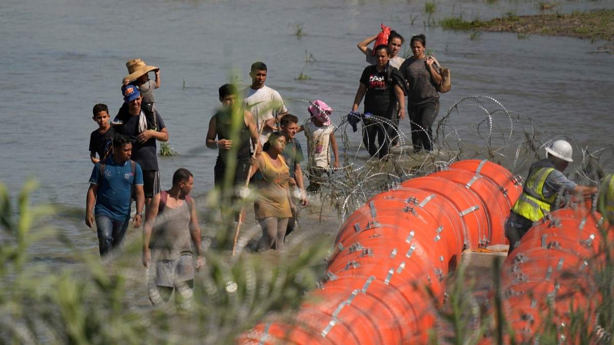 Migrantes que tratan de entrar a Estados Unidos desde México se acercan a un sitio donde trabajadores están colocando unas boyas