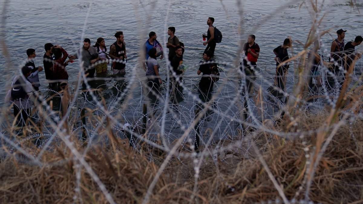 Migrantes esperan para trepar por encima del alambre de concertina después de cruzar el río Grande y entrar en Estados Unidos desde México, el 23 de septiembre de 2023, en Eagle Pass, Texas