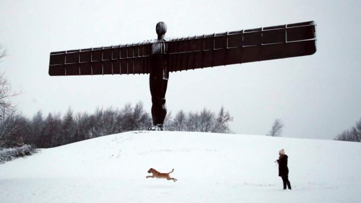 Una señora con su perro frente a la escultura de Anthony Gormley, el Ángel del Norte, que está rodeada de nieve en Gateshead, noreste de Inglaterra, mientras el mal tiempo continúa en Inglaterra, domingo 5 de enero de 2025