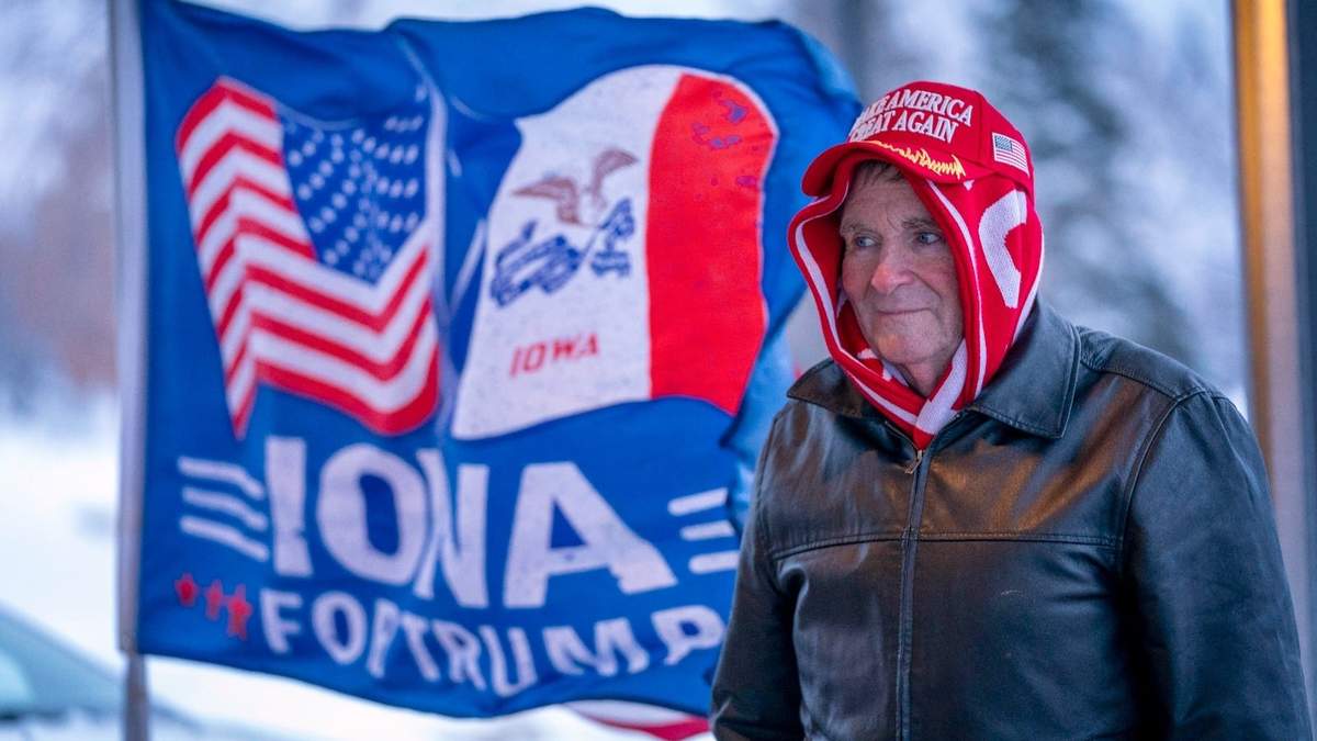 Un hombre se detiene al frente de una bandera de la campaña a favor del expresidente Donald Trump