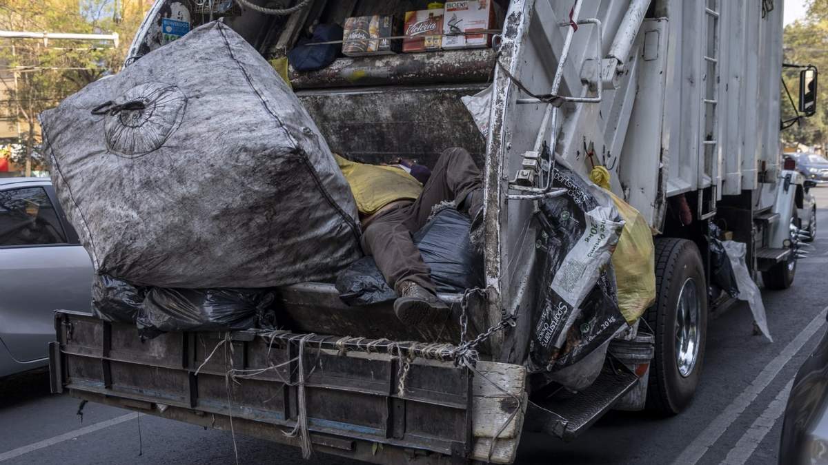Un trabajador de limpieza descansa encima de la basura en un camión recolector