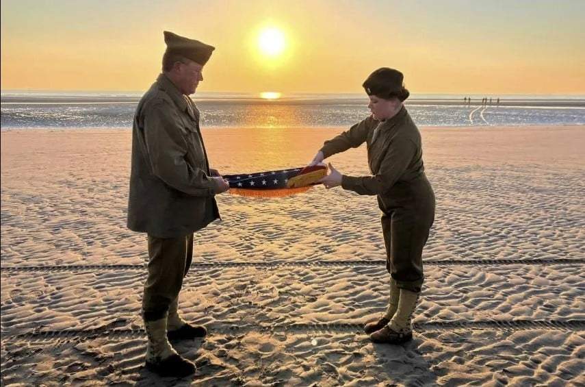 Christophe Receveur y su hija Julie, de Francia, extienden una bandera estadounidense que él compró hace seis meses en Gettysburg, Pensilvania, para conmemorar el Día D