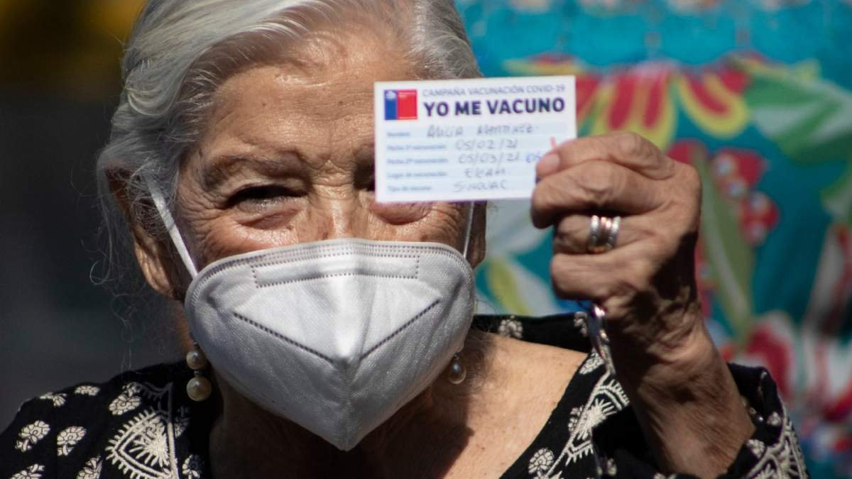 Una chilena sostiene su carnet de vacunación contra el coronavirus. Fuente: (Twitter)