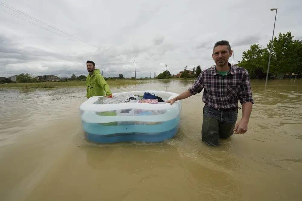 Dos hombres usan una alberca inflable para transportar sus pertenencias en un camino inundado de Lugo, Italia, el 18 de mayo de 2023