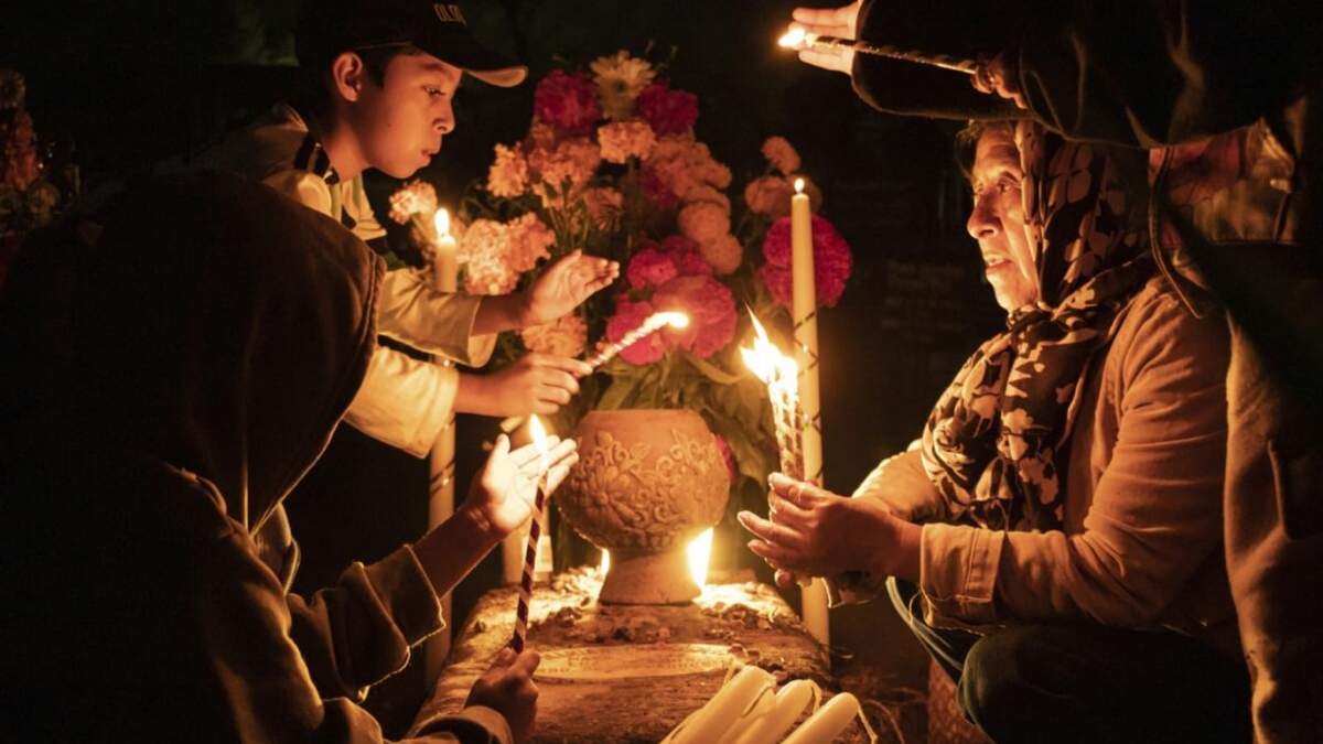 La gente sostiene velas sobre una tumba decorada con flores en un cementerio en Atzompa, México