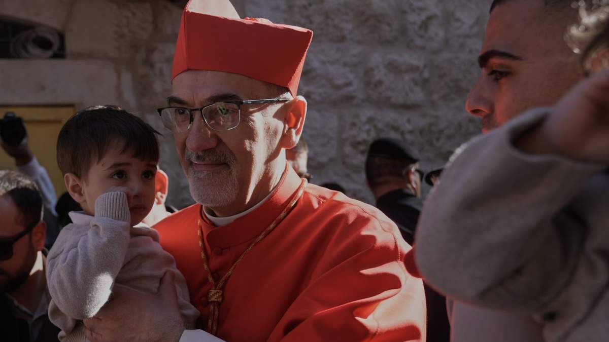 El patriarca latino Pierbattista Pizzaballa, el principal clérigo católico de Tierra Santa, sostiene a un niño mientras camina hacia la Iglesia de la Natividad, tradicionalmente considerada el lugar de nacimiento de Jesús, en Nochebuena, en la ciudad cisjordana de Belén