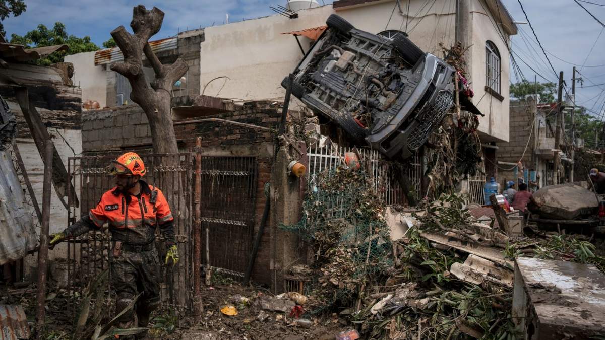Un rescatista, miembro de la brigada de voluntarios Topos, trabaja cerca de un automóvil colgado de una cerca junto a una casa dañada en Poza Rica, Veracruz