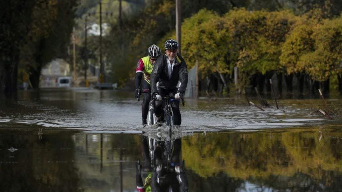 Dave Edmonds, a la derecha, y Mike Raasch transitan en bicicleta en una carretera inundada el sábado 23 de noviembre de 2024, en Windsor, California